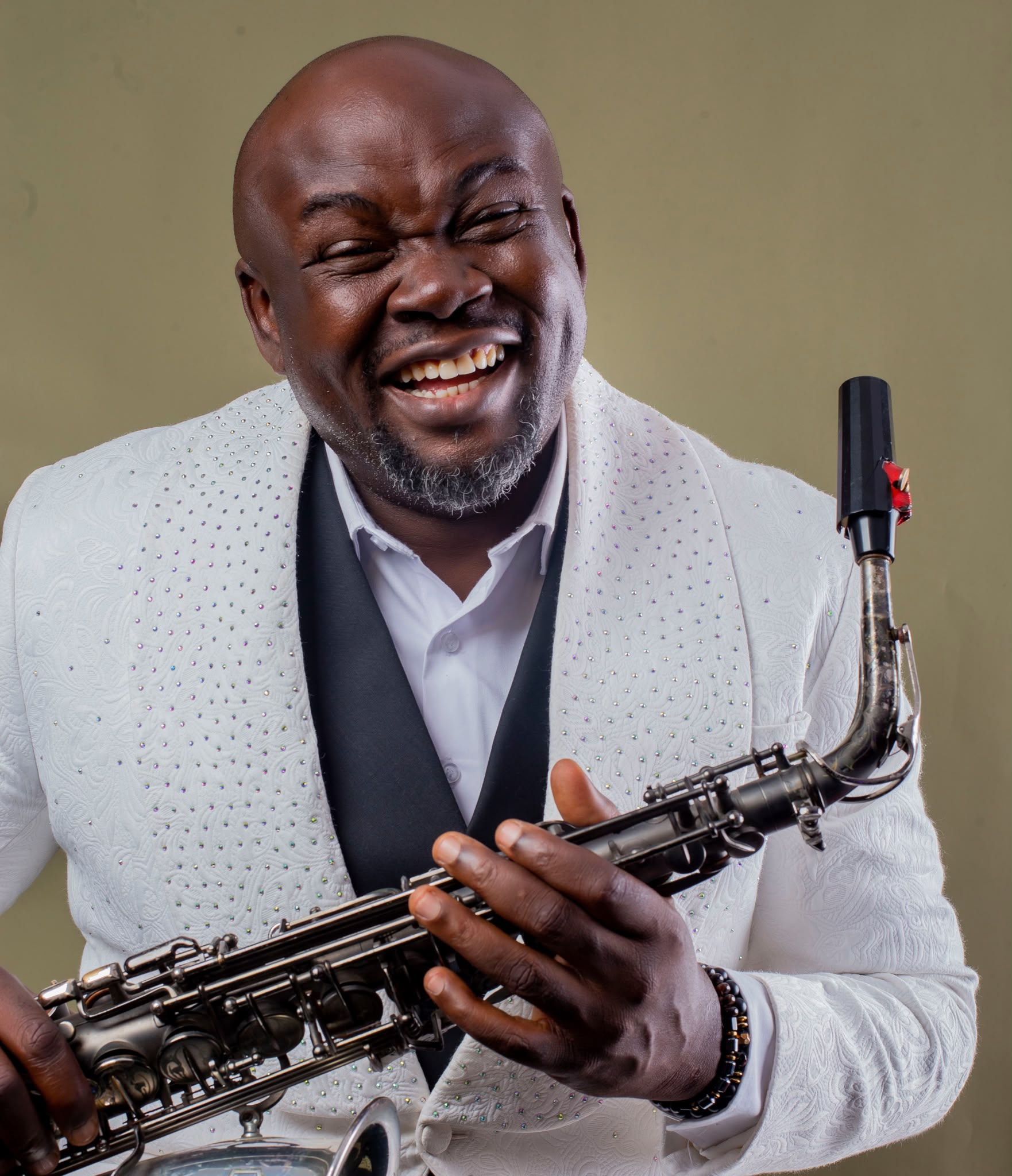 Segun Oluwayomi beaming with his saxophone in a bespoke diamond white tuxedo